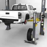 White pickup on a two-post lift with rear wheel removed, featuring Gaither Wheel Assist and sliding tire roller